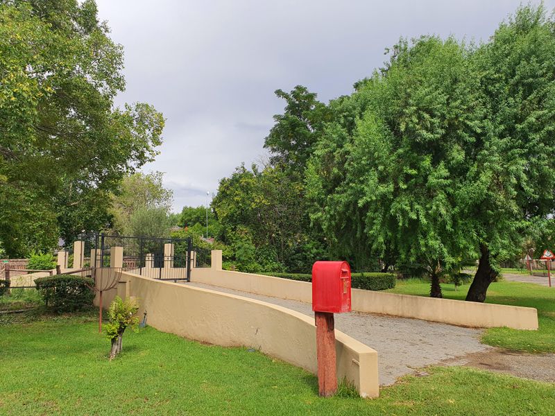 A view of the property entrance featuring a paved driveway, retaining walls, and a metal gate set within a landscaped garden area.