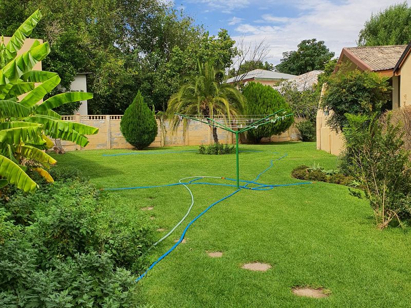 A spacious rear garden featuring a well-maintained lawn, mature trees, and a secure precast concrete boundary wall.