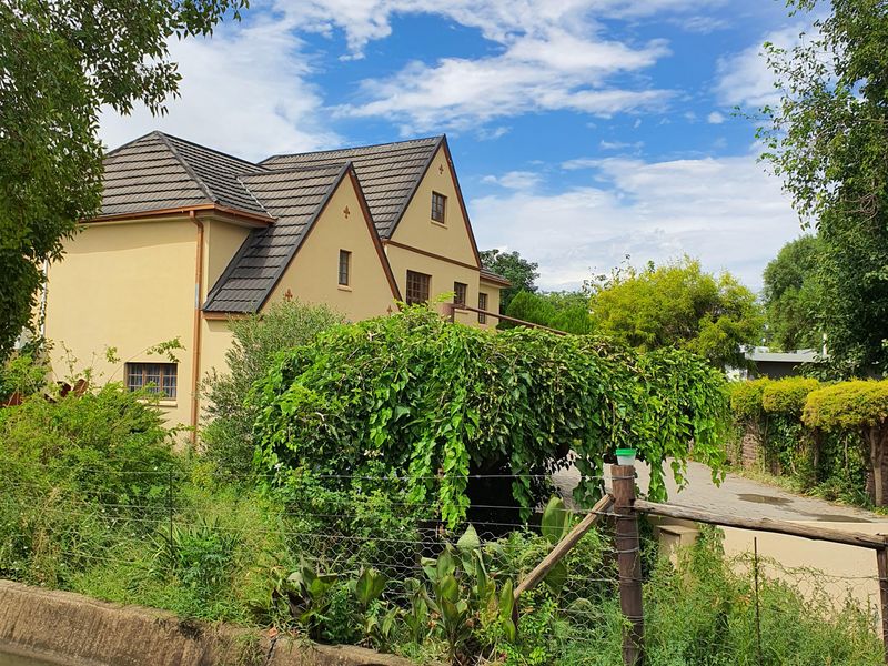 A view of the rear elevation of a multi-story house featuring a tiled roof, situated behind a concrete drainage channel and rustic fencing.