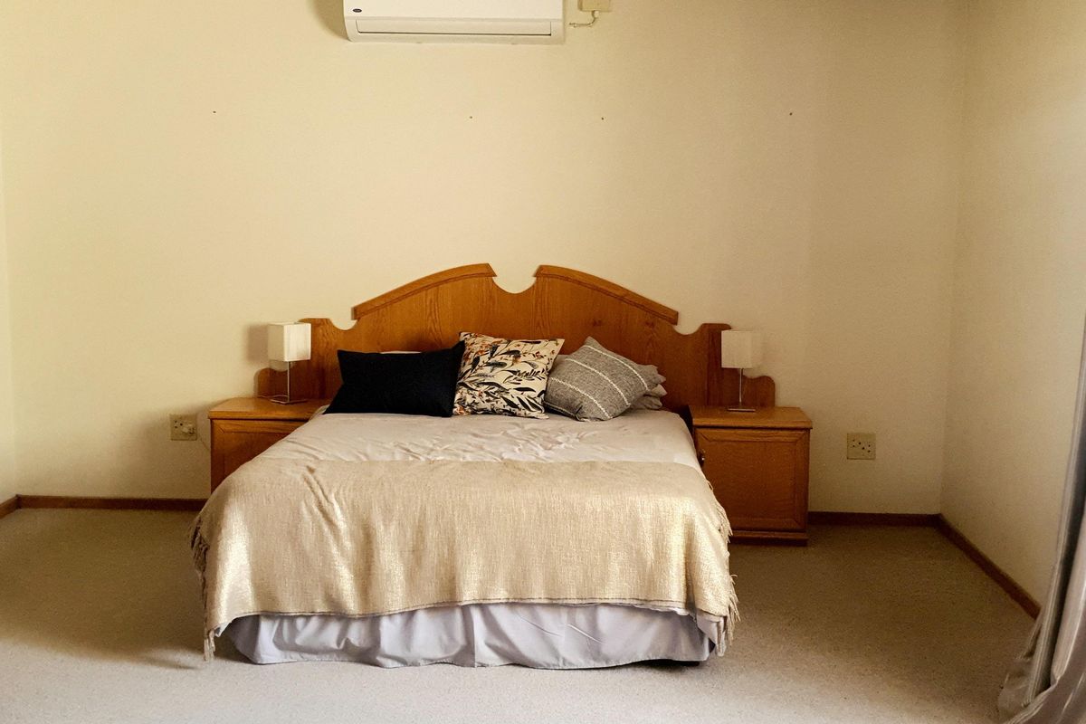 A spacious bedroom featuring neutral carpet flooring, a ceiling fan, and a wall-mounted split-system air conditioning unit.