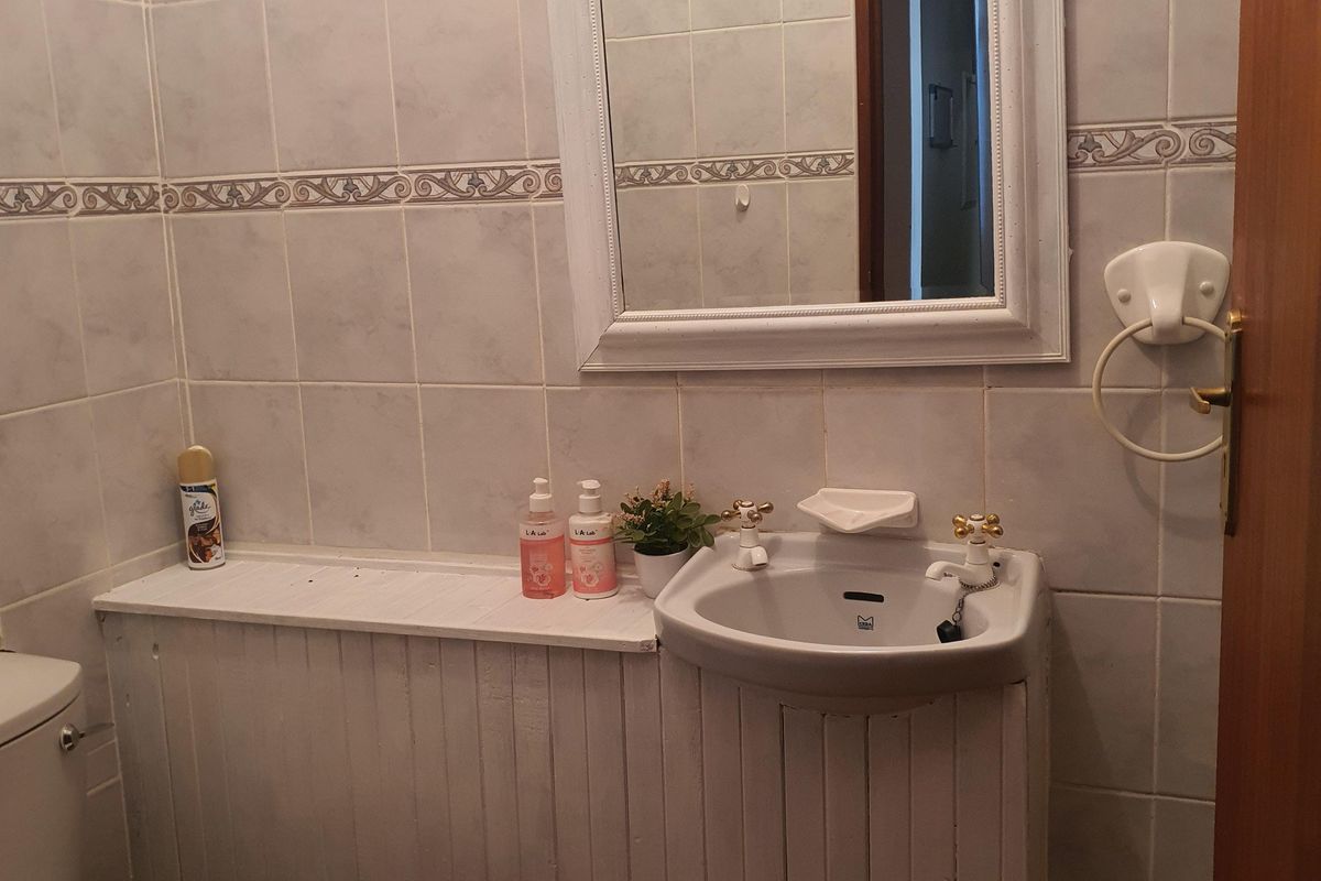 A compact bathroom featuring tiled walls, a wall-mounted mirror, a pedestal sink, and a toilet with custom timber vanity cladding.
