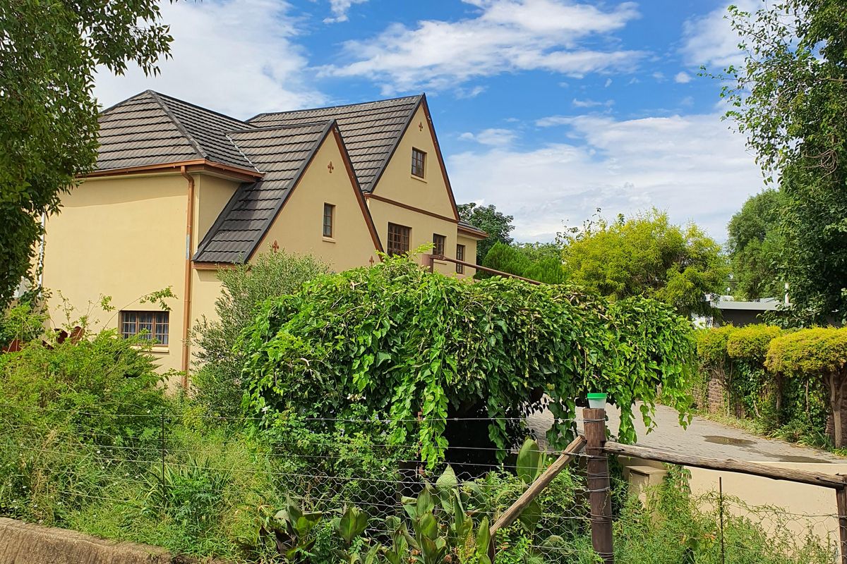 A view of the rear elevation of a multi-story house featuring a tiled roof, situated behind a concrete drainage channel and rustic fencing.