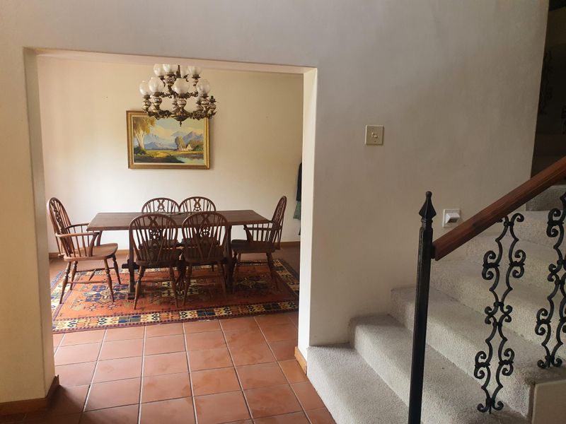 Dining area featuring terracotta floor tiles, viewed from the adjacent hallway with a carpeted staircase and decorative wrought iron railing.