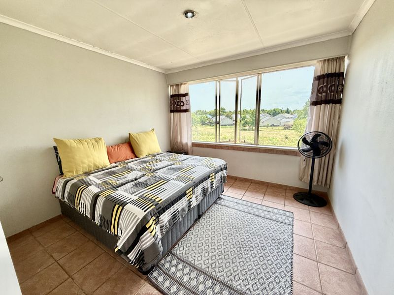 A bedroom featuring tiled flooring, a large window with natural light, and a neutral wall finish, offering a functional space with exterior views.