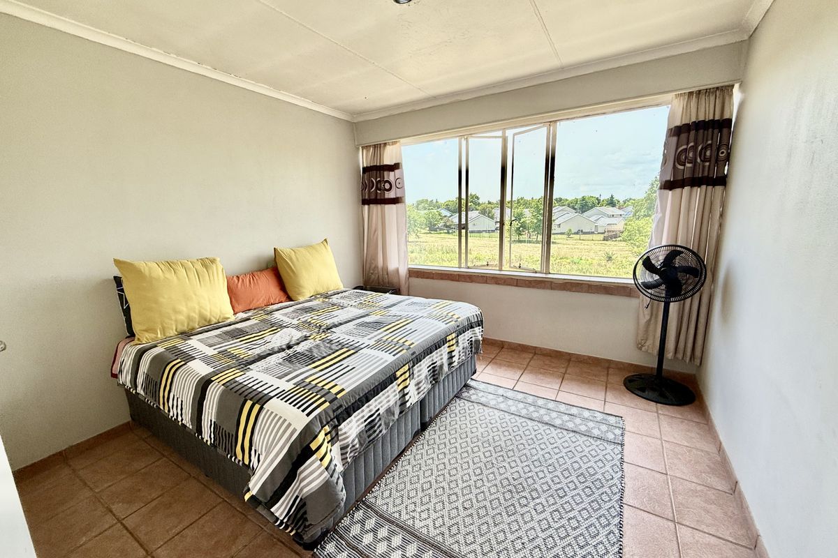 A bedroom featuring tiled flooring, a large window with natural light, and a neutral wall finish, offering a functional space with exterior views.