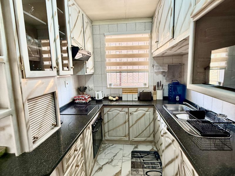 A galley-style kitchen featuring granite countertops, built-in cabinetry, an electric hob, and an integrated oven with marble-look floor tiles.