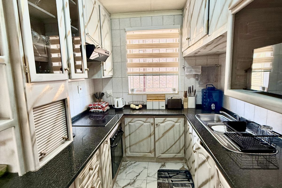 A galley-style kitchen featuring granite countertops, built-in cabinetry, an electric hob, and an integrated oven with marble-look floor tiles.