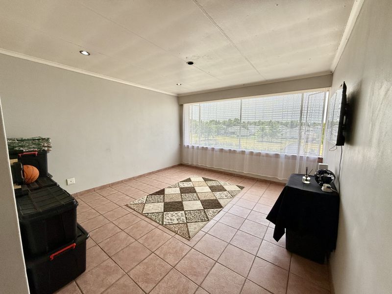 A spacious, tiled living area featuring large windows with natural light, recessed ceiling lighting, and a wall-mounted television point.
