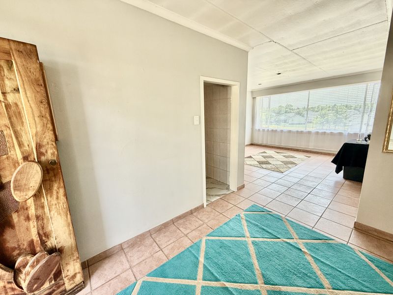 A spacious living area featuring tiled flooring, large windows for natural light, and a coved ceiling, offering a blank canvas for renovation.