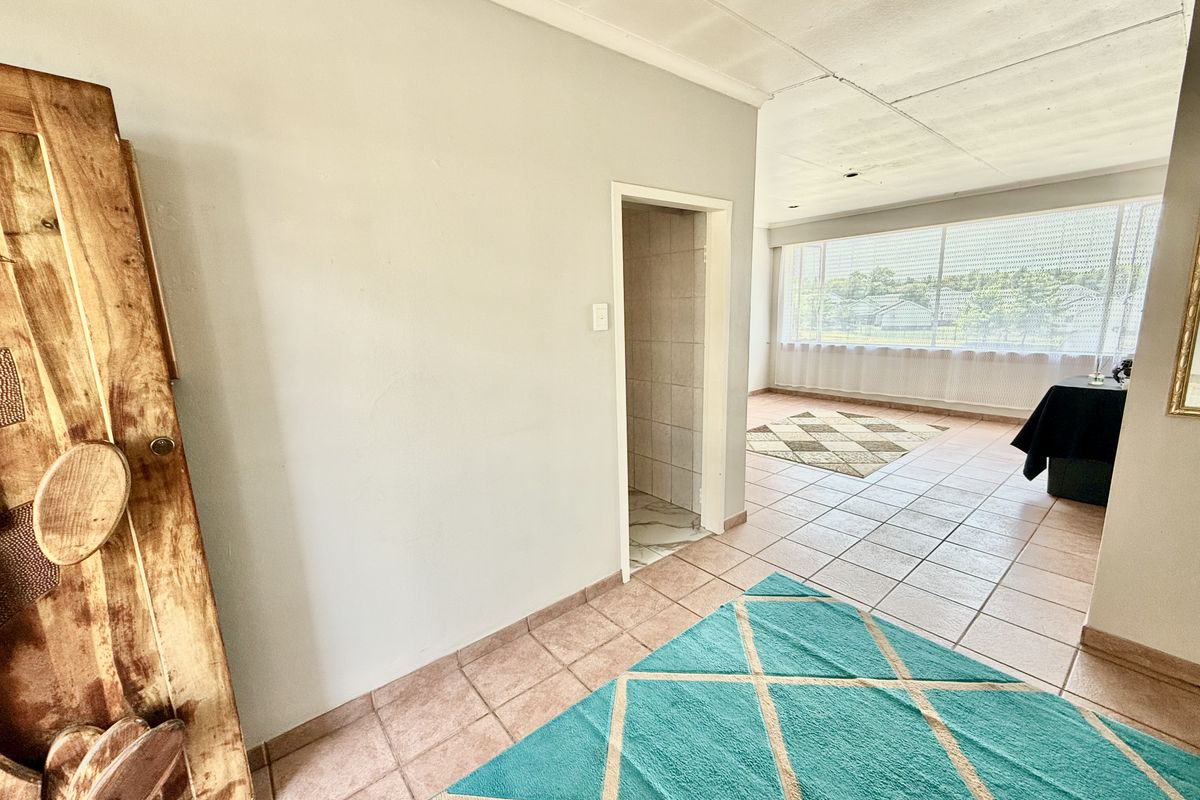 A spacious living area featuring tiled flooring, large windows for natural light, and a coved ceiling, offering a blank canvas for renovation.