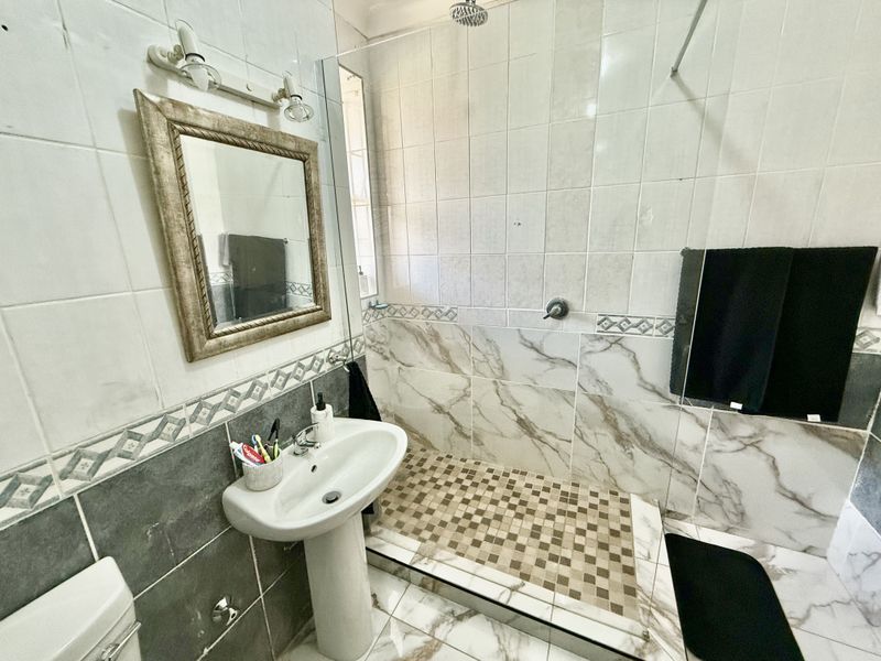 A functional bathroom featuring a pedestal washbasin, a walk-in shower with tiled flooring, and a toilet, finished with a mix of marble-effect and decorative wall tiles.