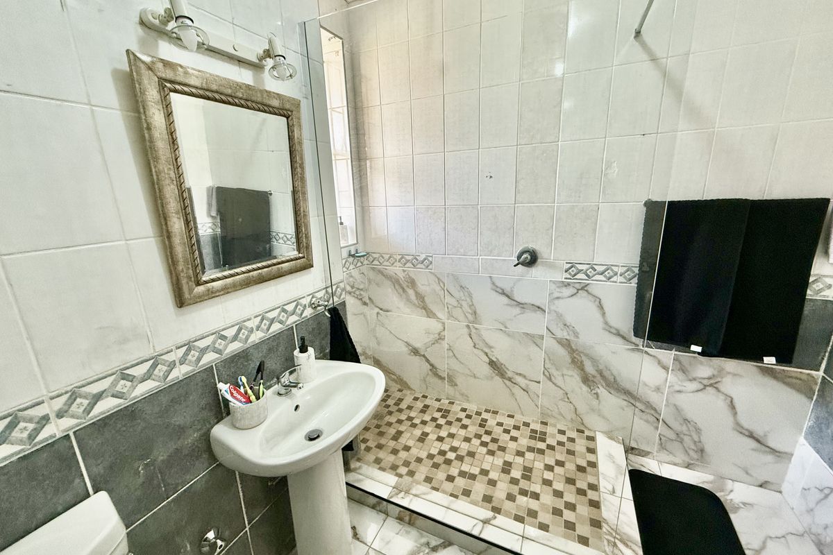A functional bathroom featuring a pedestal washbasin, a walk-in shower with tiled flooring, and a toilet, finished with a mix of marble-effect and decorative wall tiles.