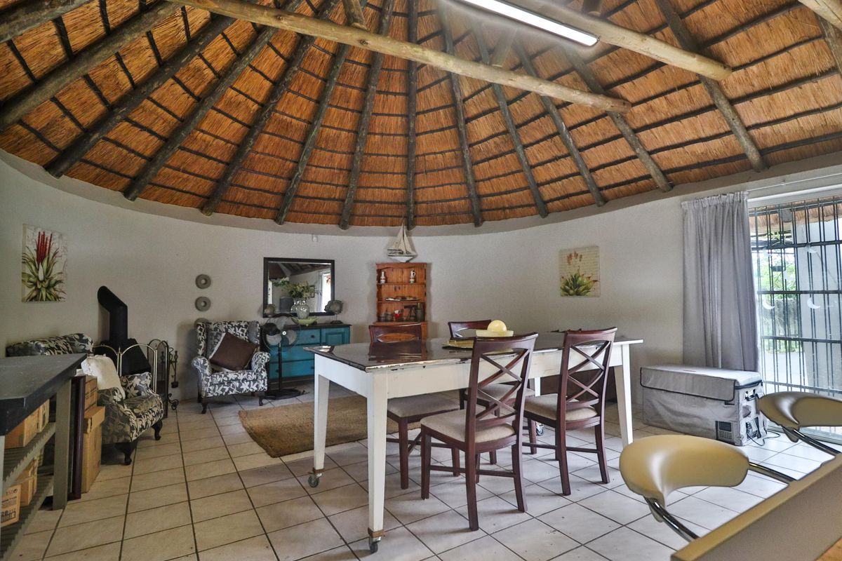 Spacious circular living area featuring a traditional thatched roof with exposed timber rafters, ceramic tiled flooring, and a built-in wood burning stove.