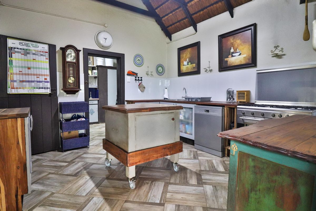 A rustic kitchen featuring a high-pitched thatch roof with exposed beams, tiled flooring, and functional built-in cabinetry with a gas stove.