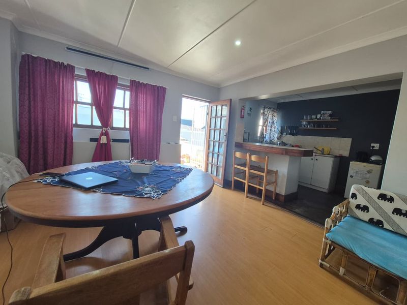 Open-plan living and dining area featuring a breakfast bar, kitchen cabinetry, and laminate flooring with direct access to an outdoor space.
