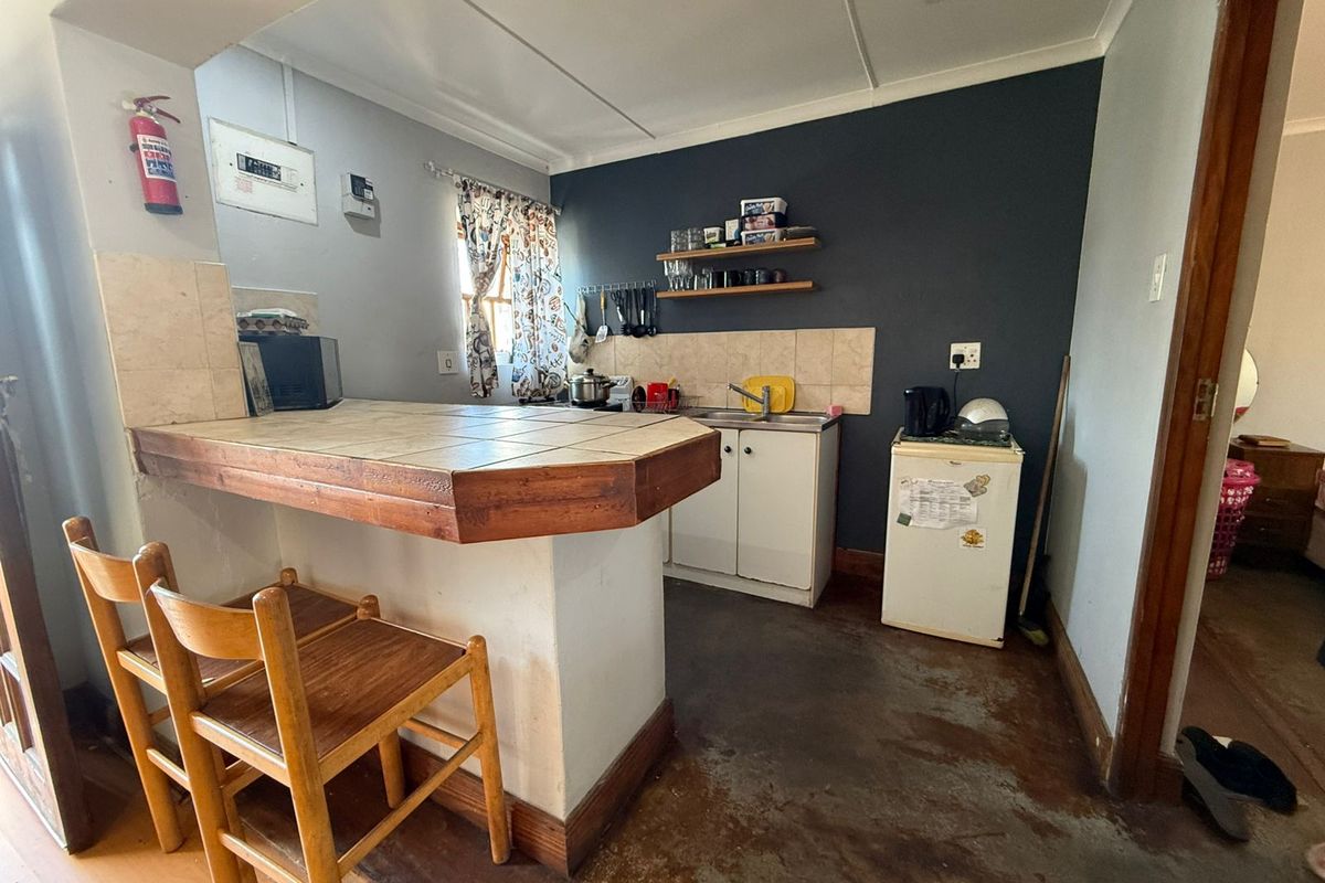 Compact kitchen featuring a tiled breakfast bar, base cabinetry, and a tiled splashback, requiring cosmetic updates to improve the overall finish.