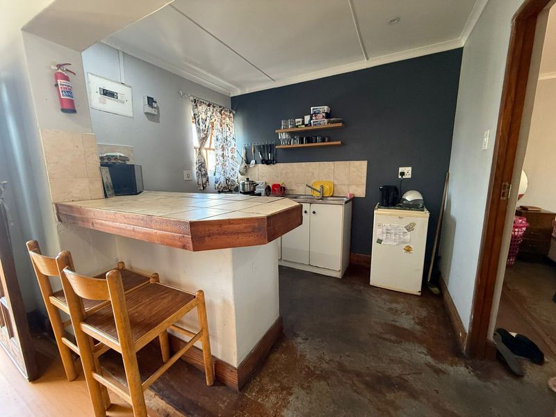 Compact kitchen featuring a tiled breakfast bar, base cabinetry, and a tiled splashback, requiring cosmetic updates to improve the overall finish.
