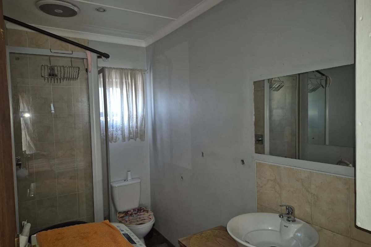 A functional bathroom featuring a shower enclosure, toilet, and vanity basin with a wall-mounted mirror, requiring minor cosmetic updates to the wall finishes.