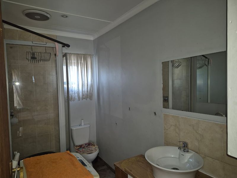 A functional bathroom featuring a shower enclosure, toilet, and vanity basin with a wall-mounted mirror, requiring minor cosmetic updates to the wall finishes.