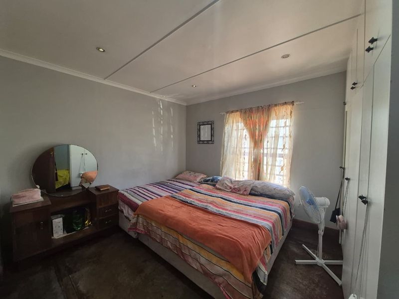 A bedroom featuring built-in cupboards, recessed downlighting, and security bars on the window.