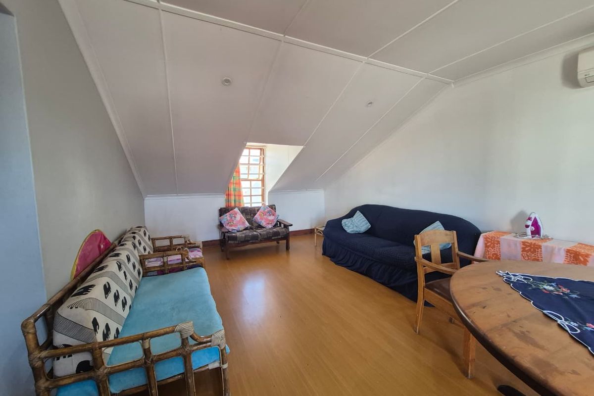 Spacious living area featuring laminate flooring, a pitched ceiling, and a wall-mounted air conditioning unit, offering a versatile layout for relaxation.