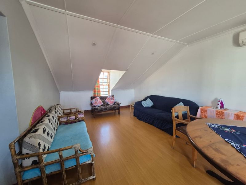 Spacious living area featuring laminate flooring, a pitched ceiling, and a wall-mounted air conditioning unit, offering a versatile layout for relaxation.
