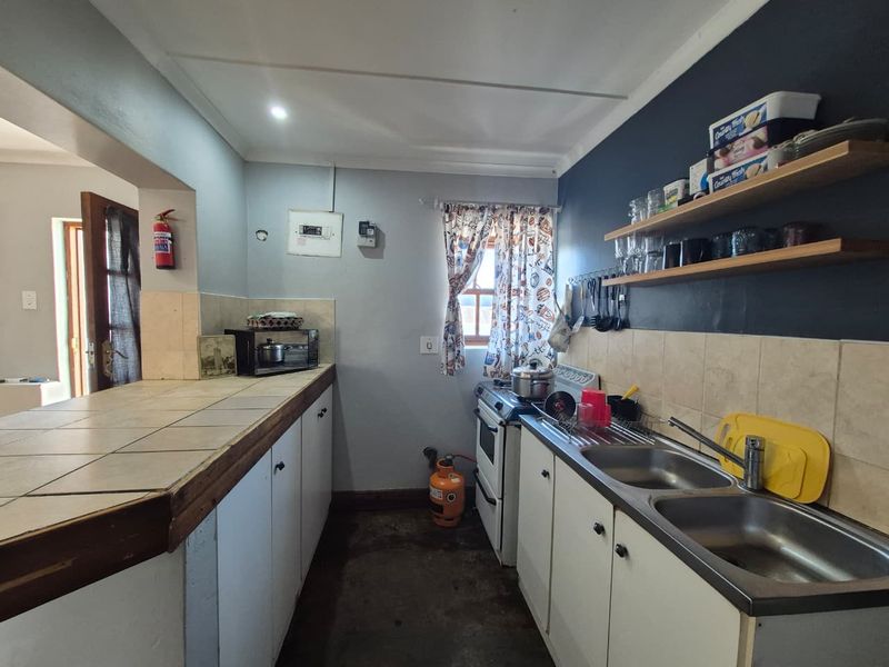 A functional kitchen featuring tiled countertops, a double basin sink, gas stove, and open shelving, offering potential for modernization and aesthetic improvement.