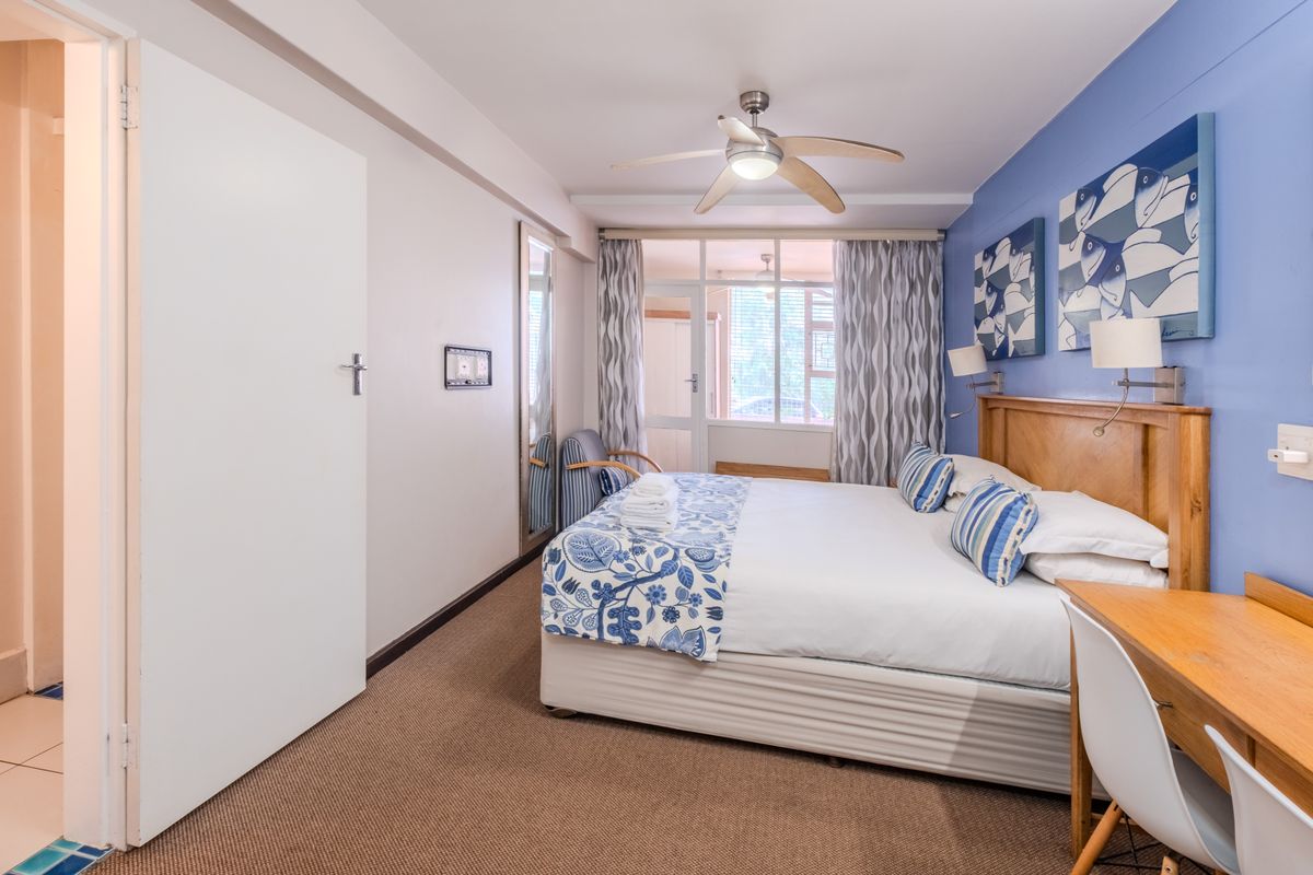 A well-lit bedroom featuring a ceiling fan, carpeted flooring, and direct access to a private balcony through a sliding glass door.