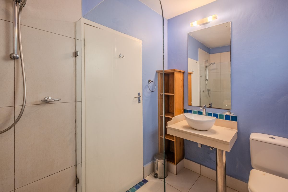 A functional bathroom featuring a glass-enclosed shower, a modern vessel sink on a pedestal vanity, and a standard toilet with blue painted walls.