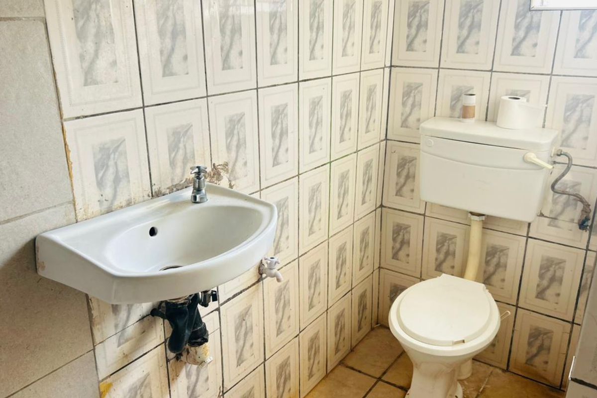 A compact bathroom featuring a wall-mounted basin and standard toilet, requiring renovation to update the dated tiling and fixtures.