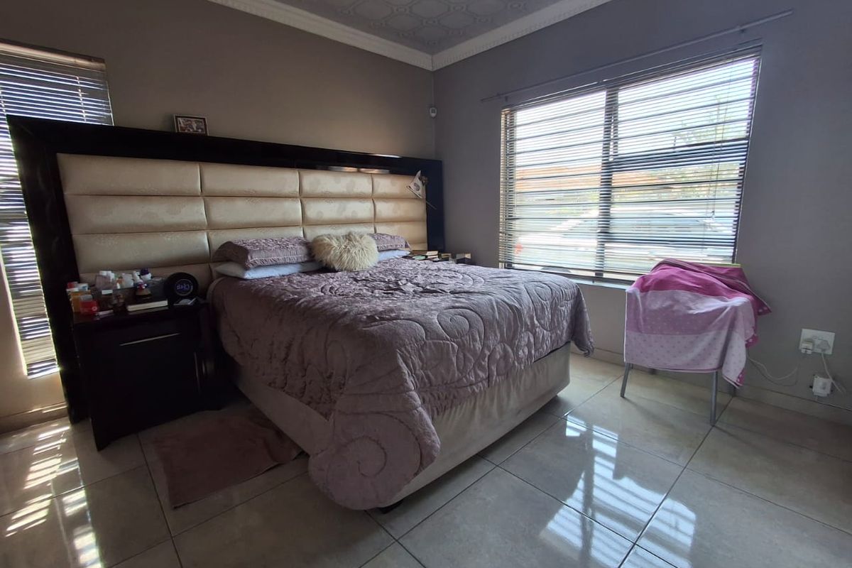 A bedroom featuring tiled flooring, decorative ceiling molding, and venetian blinds, with a large built-in headboard as the focal point.
