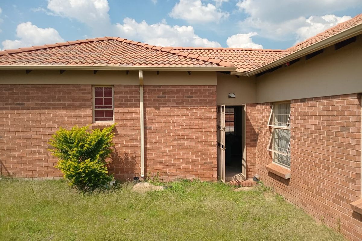 Rear view of the townhouse featuring a facebrick facade, terracotta tiled roof, and a secure entrance door leading into the property.