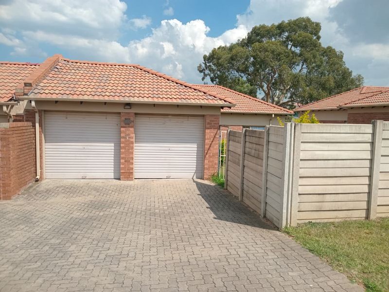 Front exterior view of a townhouse featuring a double garage with roll-up doors, a paved driveway, and a tiled roof.