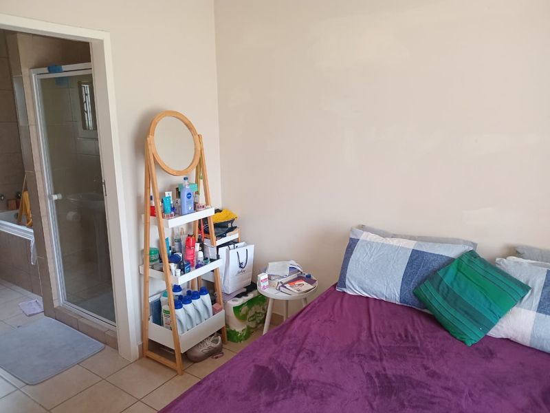 A bedroom featuring tiled flooring and an adjoining en-suite bathroom equipped with a shower enclosure and a built-in bathtub.