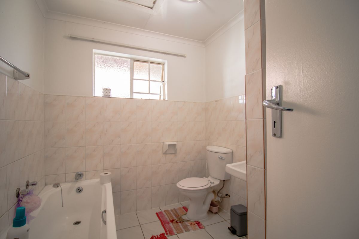 A functional bathroom featuring a bathtub, toilet, and wall-mounted basin with neutral wall and floor tiling.