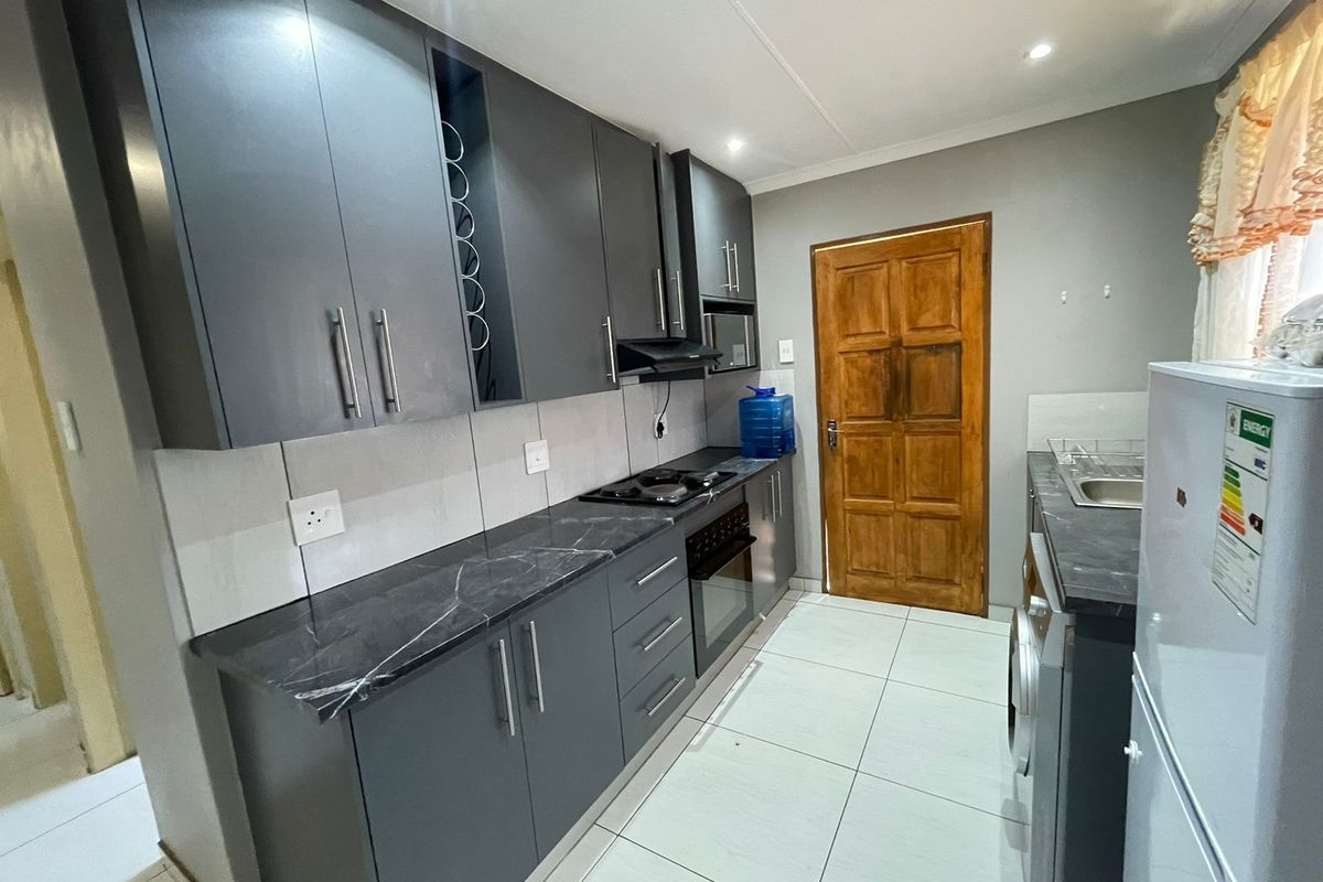 Modern kitchen featuring dark grey cabinetry, marble-effect countertops, built-in oven, hob, extractor fan, and tiled flooring.