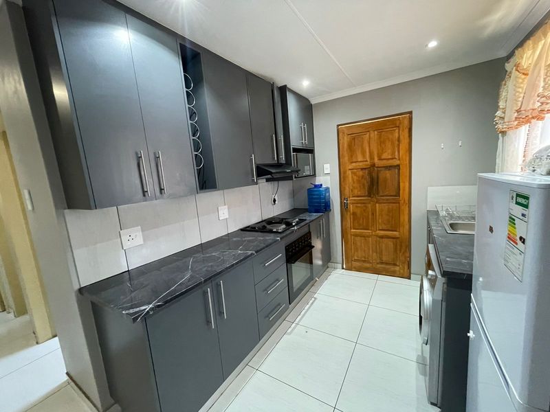 Modern kitchen featuring dark grey cabinetry, marble-effect countertops, built-in oven, hob, extractor fan, and tiled flooring.