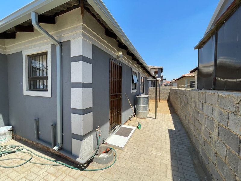 A side exterior view of the property featuring paved walkways, a security gate, and a boundary wall.