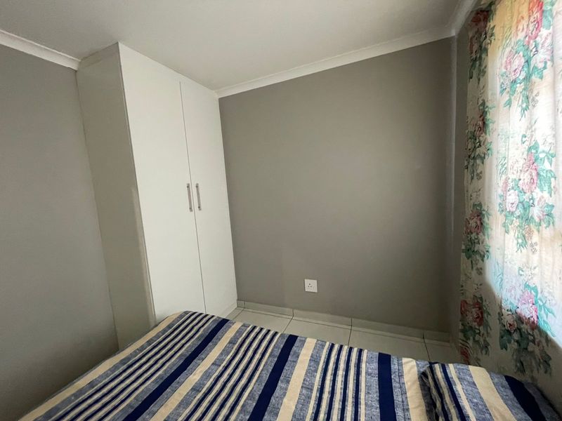 A bedroom featuring neutral grey walls, tiled flooring, and a white built-in wardrobe.
