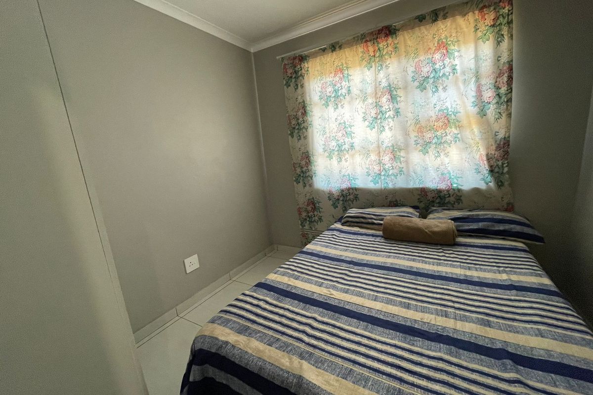 A functional bedroom featuring neutral wall finishes, tiled flooring, and a built-in cupboard, offering a clean and simple living space.