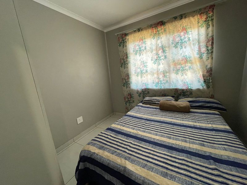 A functional bedroom featuring neutral wall finishes, tiled flooring, and a built-in cupboard, offering a clean and simple living space.