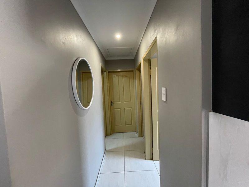 A clean and well-maintained hallway featuring neutral wall tones, tiled flooring, and recessed ceiling lighting, providing access to multiple rooms.