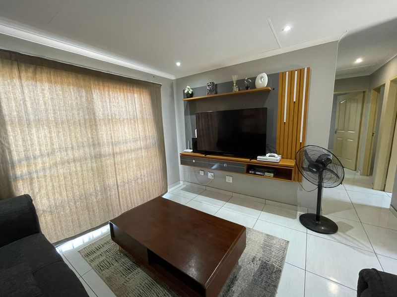 A modern living room featuring a built-in media console, tiled flooring, and recessed ceiling lighting, providing a clean and functional space.
