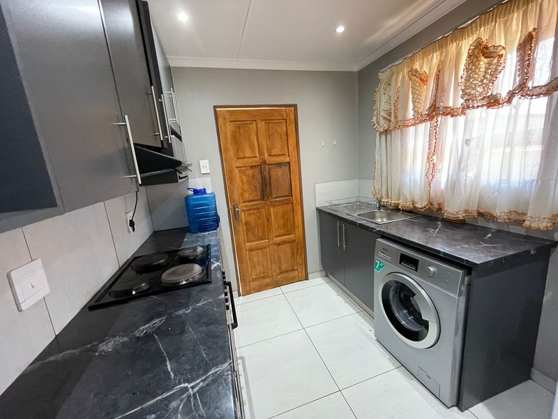 A functional kitchen featuring dark cabinetry, marble-effect countertops, an electric hob, and tiled flooring, providing a clean and practical workspace.