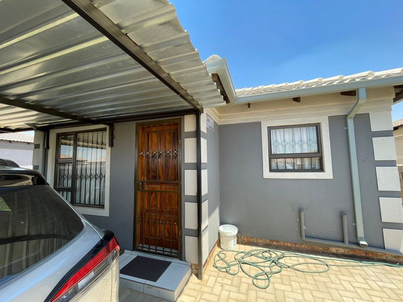 Front exterior view of the house featuring a covered carport, paved driveway, and secure entrance with a wooden door and security gate.