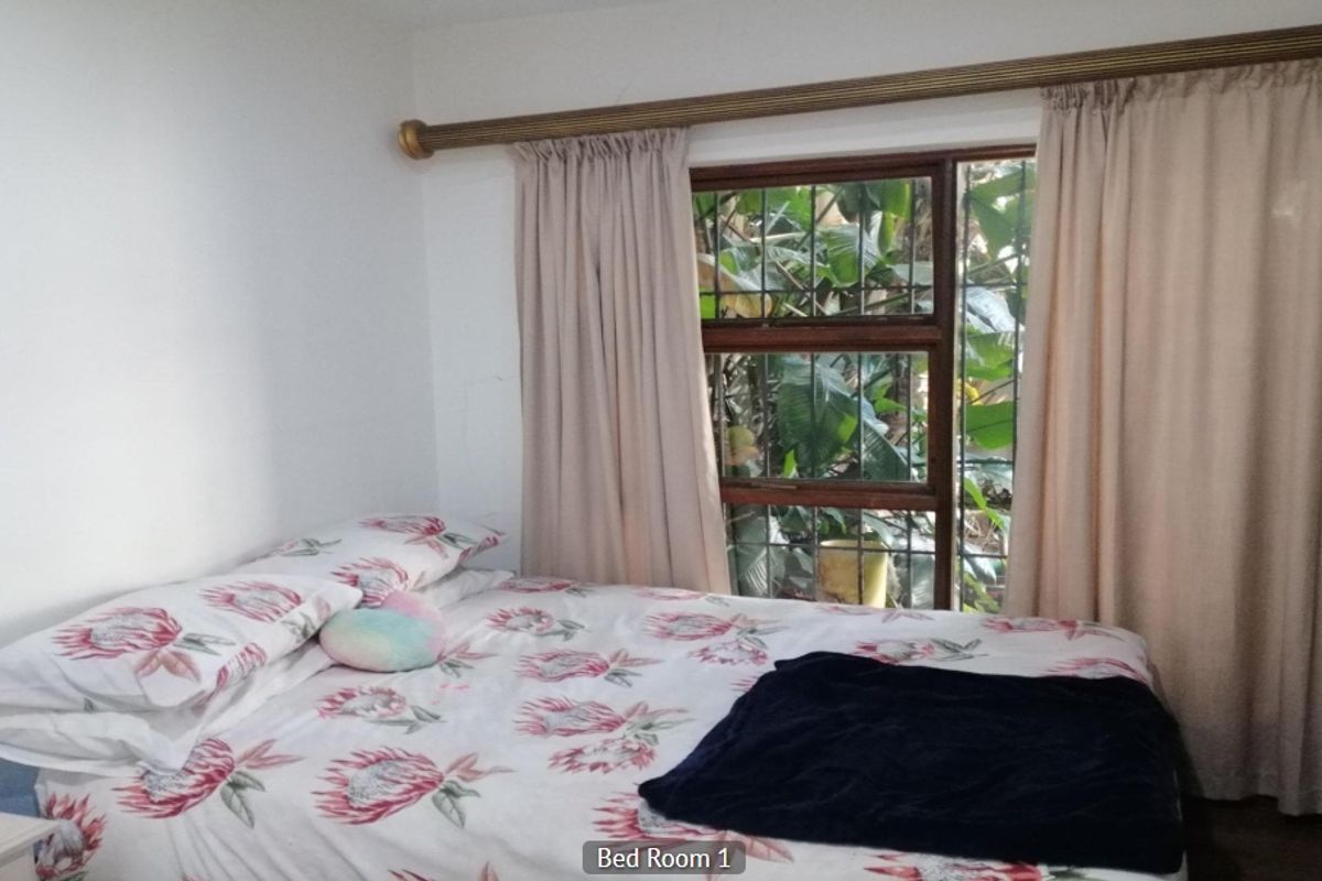 A bedroom featuring a window with security bars and a curtain rod, providing natural light and garden views.