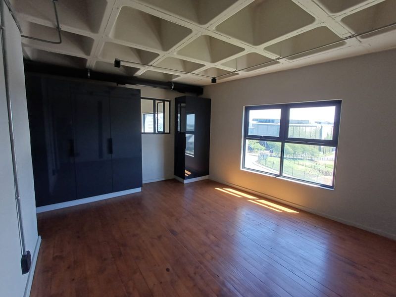Spacious bedroom featuring unique waffle slab ceiling, polished timber flooring, and modern dark built-in cupboards with large windows providing natural light.