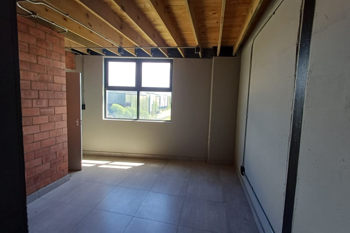 An empty bedroom featuring industrial-style exposed timber ceiling joists, an exposed brick feature wall, tiled flooring, and exposed electrical conduit.