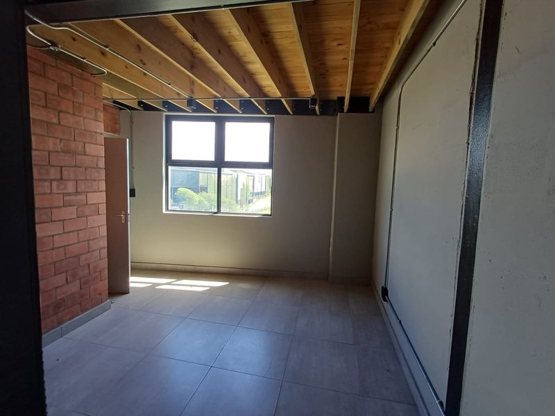 An empty bedroom featuring industrial-style exposed timber ceiling joists, an exposed brick feature wall, tiled flooring, and exposed electrical conduit.