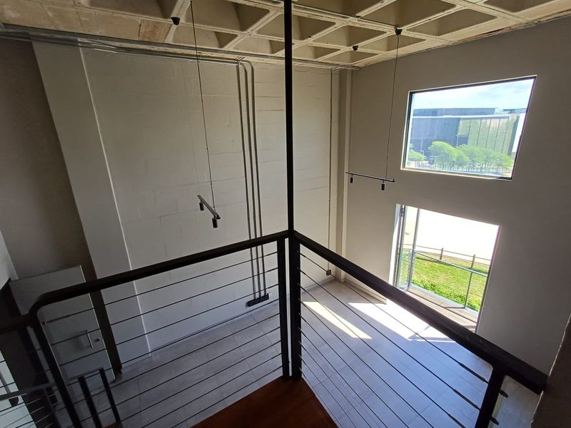Spacious double-volume living area featuring an industrial-style waffle slab ceiling, exposed conduit, and large windows providing abundant natural light and outdoor views.